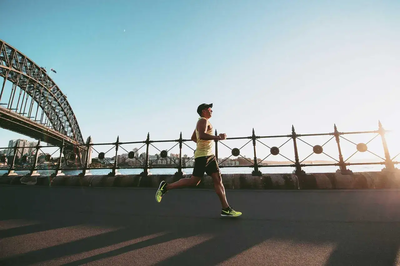 Mann im Laufschritt am Morgen, ein leichter recovery run mit Blick auf die Sydney Harbour Bridge.