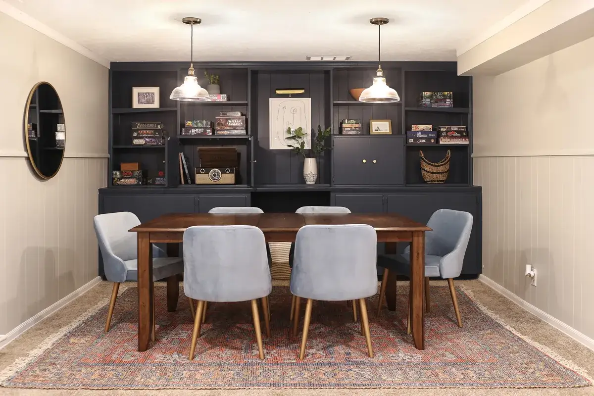Table en bois, chaises bleues, étagères remplies de jeux de société et d'objets décoratifs. Une pièce parfaite pour une salle de jeux conviviale.