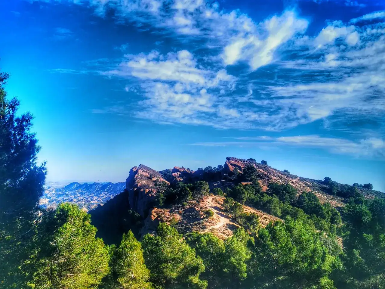 Senderos serpenteantes en la **sierra de carrascoy**, bajo un cielo azul vibrante con nubes algodonosas.