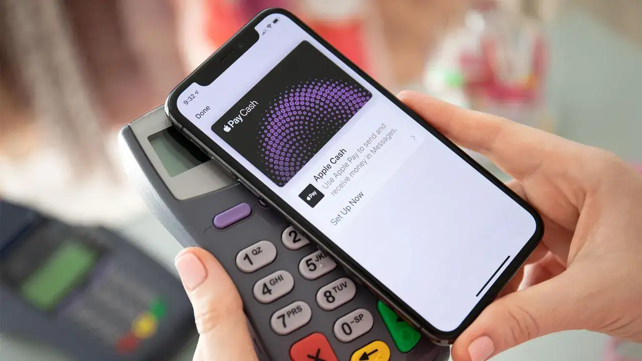 Dłoń trzyma iPhone'a nad terminalem płatniczym, pokazując ekran z informacją 