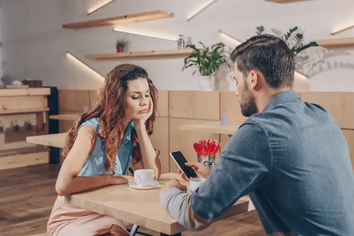 Pareja en un caf&eacute;, ella aburrida, &eacute;l absorto en su m&oacute;vil, un claro ejemplo de infidelidad emocional.