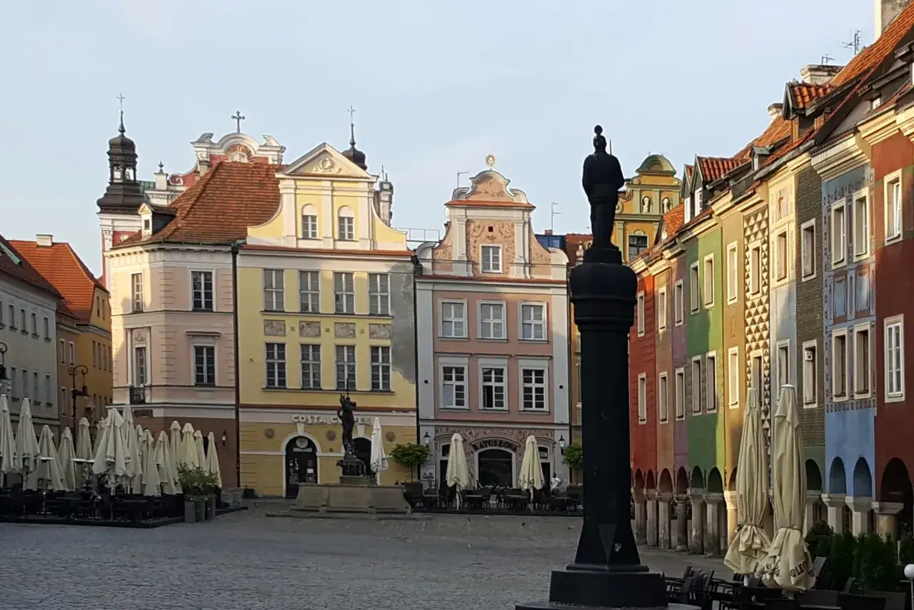 Kolorowe kamienice na poznańskim rynku, pomnik i zamknięte ogródki kawiarniane.