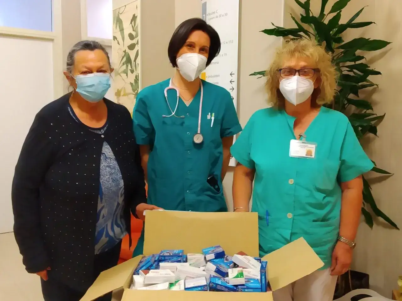 Tre donne con mascherine, due in camice verde, mostrano una scatola piena di medicinali. Un esempio di come funziona una RSA.