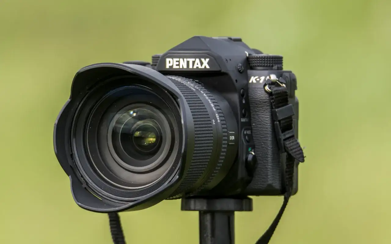 Czarny aparat Pentax K-1, zaawansowany pentax pełna klatka, z obiektywem na statywie, na tle zieleni.