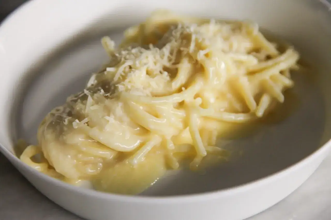 Un piatto di pasta in bianco cremosa, condita con abbondante parmigiano grattugiato, servita in una ciotola bianca.