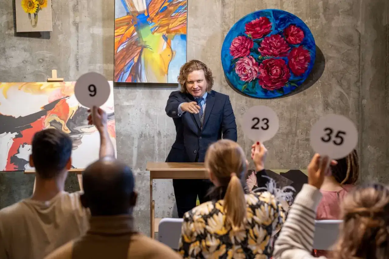 An auctioneer points to bidders holding paddles with numbers 9, 23, and 35, showcasing the dynamic art market definition in action.