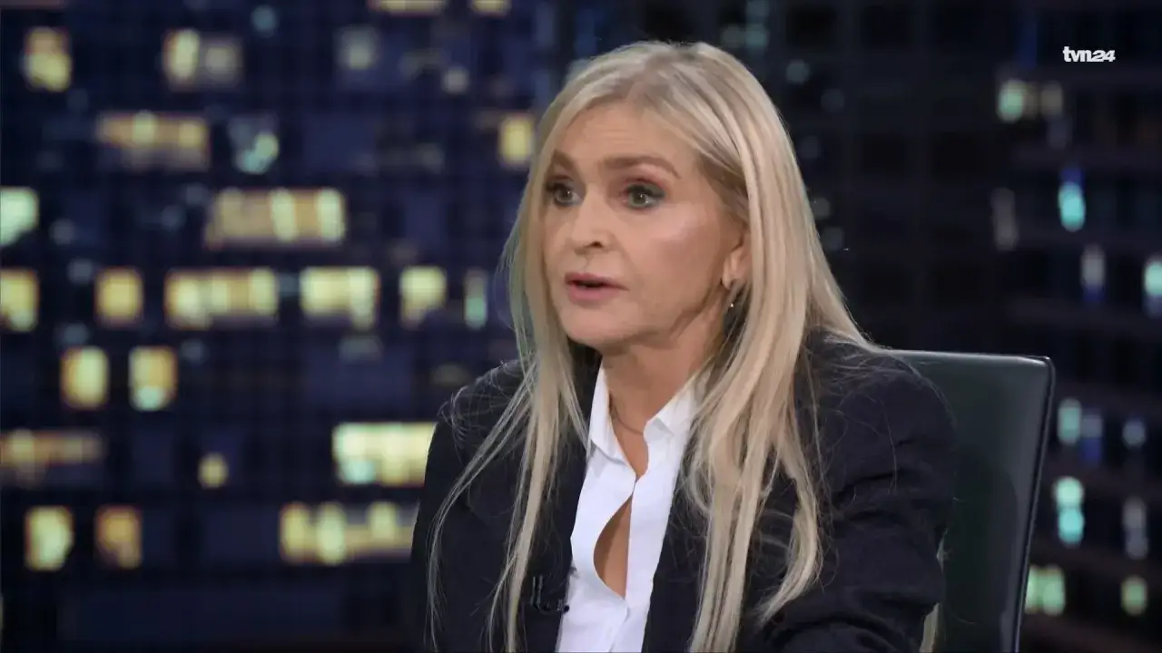 Blond prezenterka TVN24 w białej koszuli i granatowej marynarce, w tle nocne miasto.