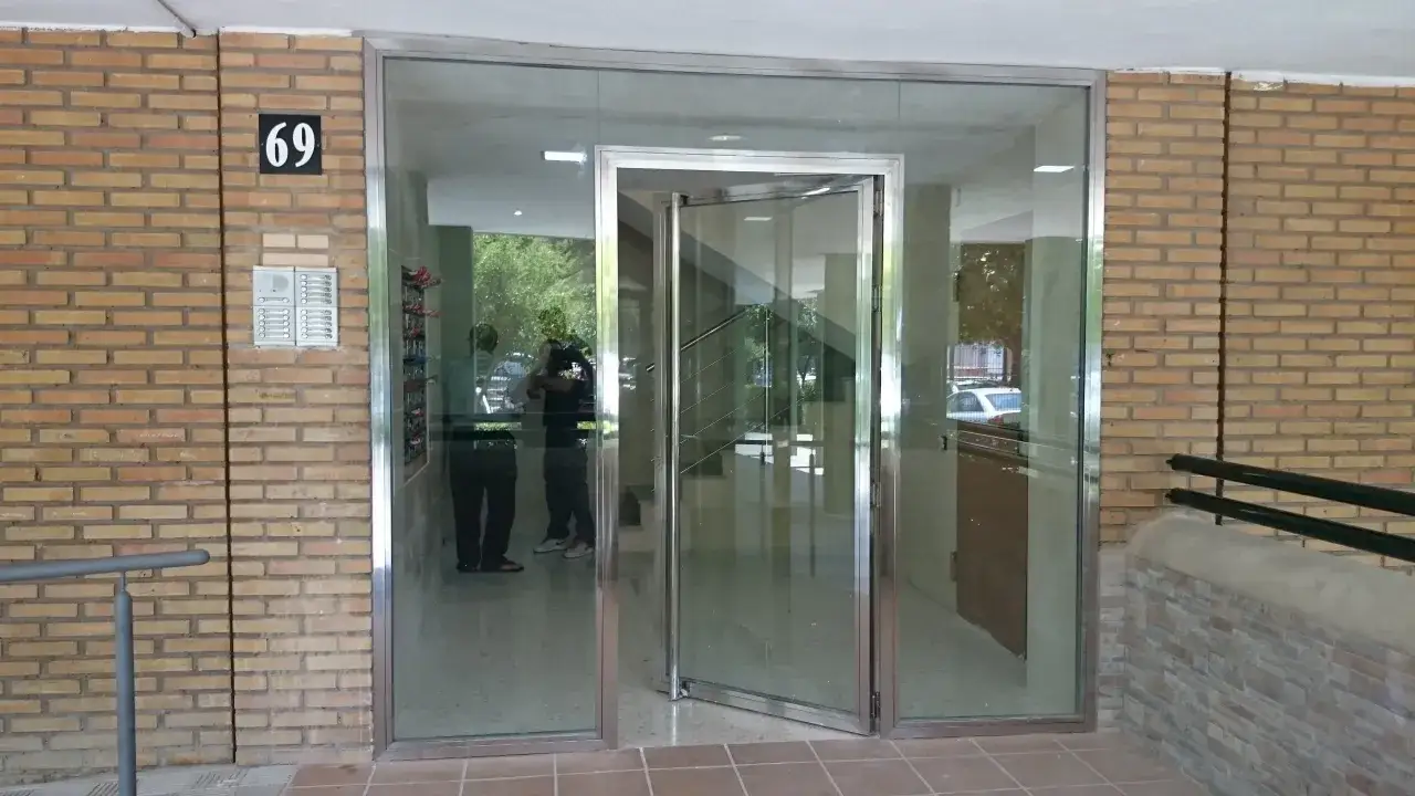 Entrada de portal con puerta acristalada y número 69. Cumple la normativa de puertas de portales para accesibilidad.