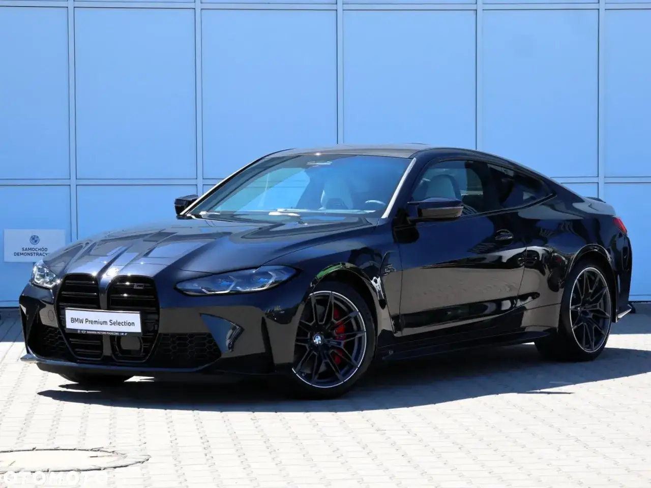 Czarny BMW M4 Competition na tle niebieskiej ściany. Sprawdź aktualną bmw m4 cena i ofertę.