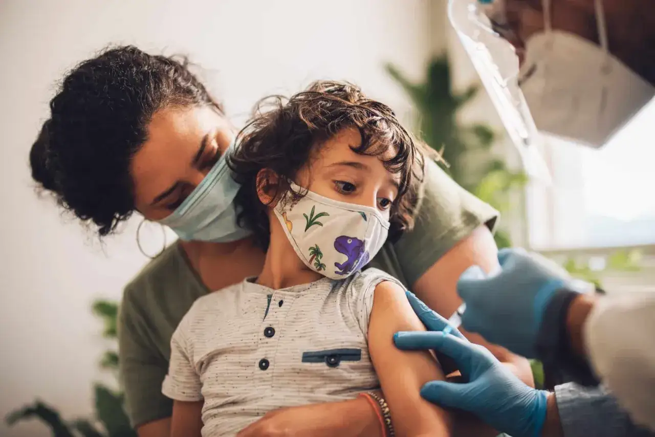 Madre abraza a su hijo mientras recibe una vacuna. Es recomendable vacunar a los niños de la gripe para proteger su salud.