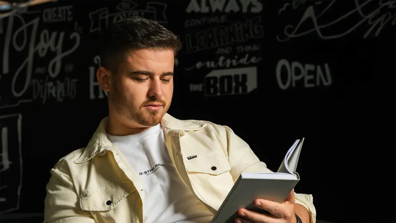 Junger Mann liest ein Buch, das ihm hilft, als Unternehmer zu wachsen. Die Wand hinter ihm ist mit inspirierenden Zitaten wie 