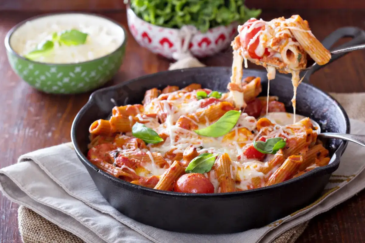 Penne z sosem pomidorowym i ciągnącym serem, idealne co do warzyw na patelnie. Podane w żeliwnej patelni, ozdobione bazylią.