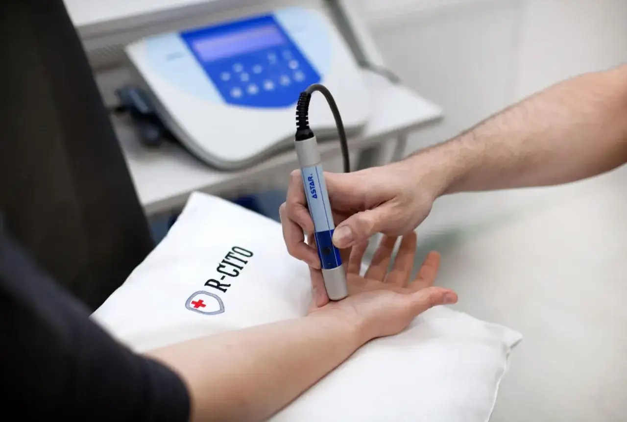 Fizjoterapeuta aplikuje pole magnetyczne na dłoń pacjenta, wspomagając leczenie.
