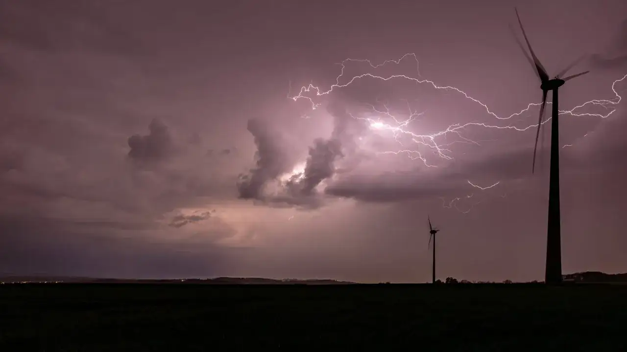 Gewaltiger Blitz zuckt über den Himmel, während zwei Windräder im Sturm stehen. Ein **orkan**-artiges Naturschauspiel.