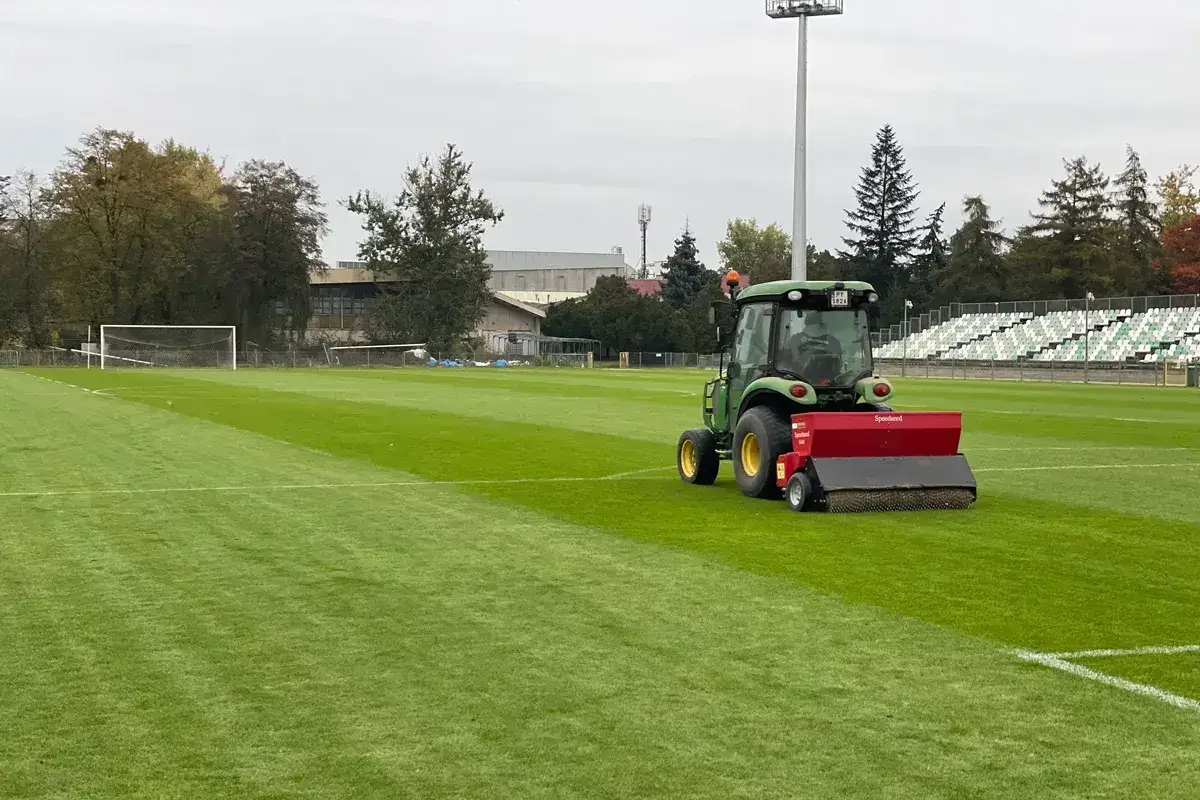 Traktor z siewnikiem pracuje na boisku, pokazując, jak dosiewać trawę, by murawa była idealna.