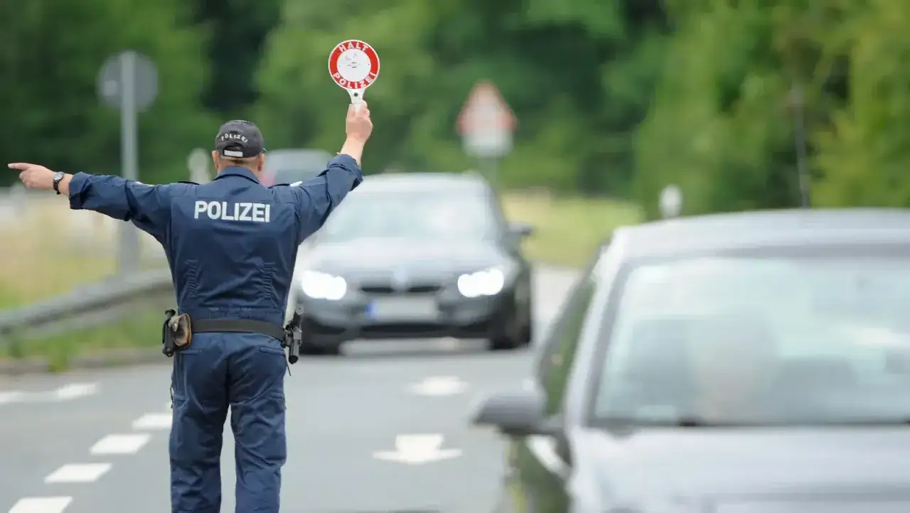 Polizist regelt Verkehr mit Stoppschild. Ein Auto hält an, ein anderes fährt langsam vorbei. 47.