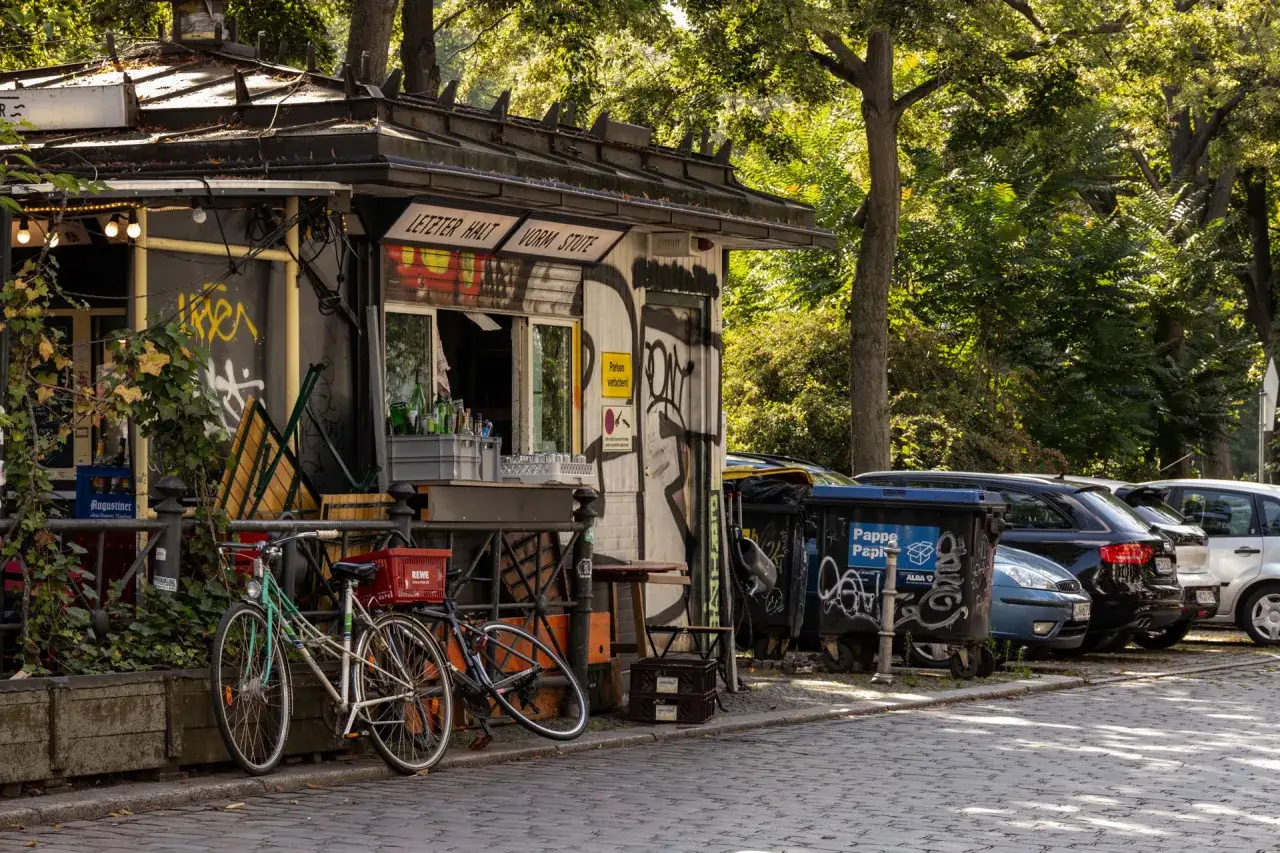Ein Kiosk mit Graffiti in Berlin Kreuzberg, Fahrr&auml;der und Autos parken davor.