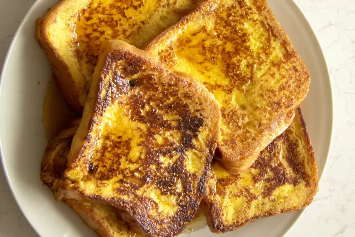 Des tranches dorées de pain perdu au four, nappées de sirop, sur une assiette blanche. Un délice pour le petit-déjeuner.