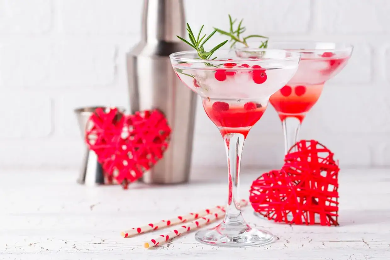 Deux cocktails sans alcool Saint-Valentin, d&eacute;cor&eacute;s de baies rouges et de romarin, avec des c&oelig;urs rouges et des pailles festives.