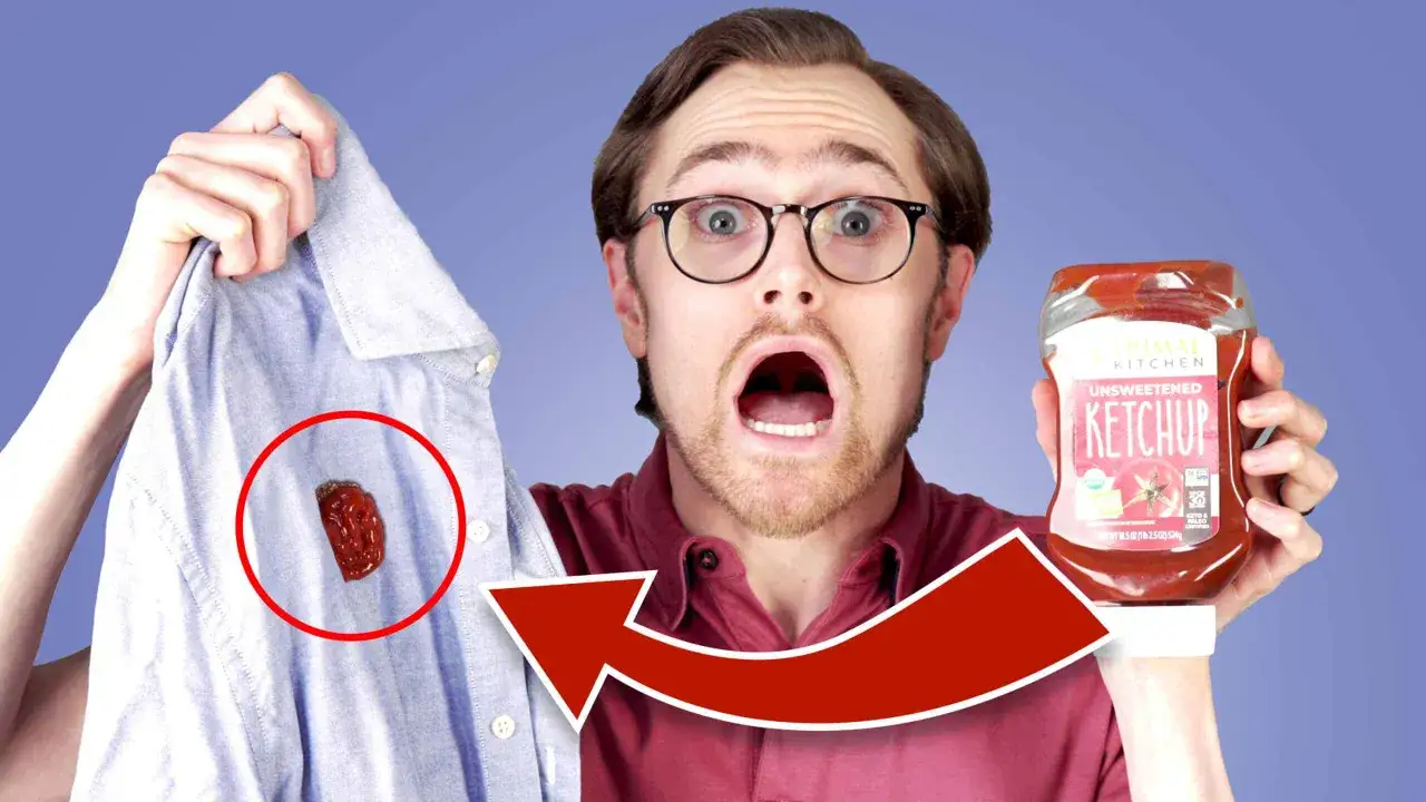 Mężczyzna z przerażoną miną pokazuje koszulę z plamą z pomidora i butelkę ketchupu.