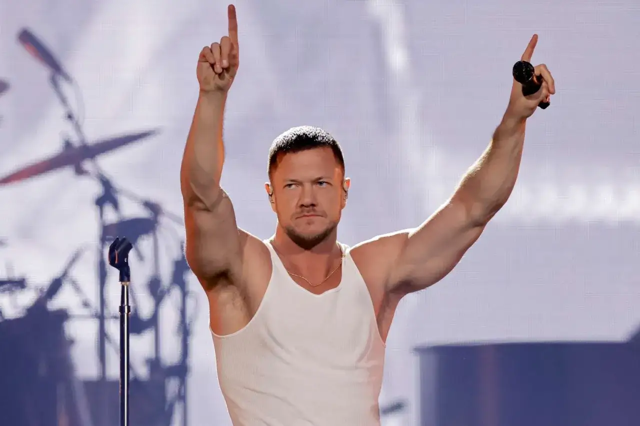 Imagine Dragons wokalista Dan Reynolds z uniesionymi ramionami i palcami wskazującymi w g&oacute;rę, śpiewa na koncercie.