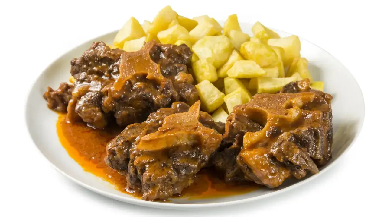 Plato de rabo de ternera estofado en salsa, acompañado de patatas fritas doradas.