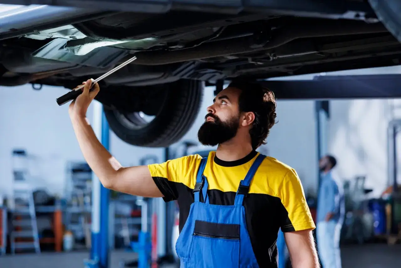 Mechanik bada podwozie auta latarką. Zastanawiasz się, ile kosztuje przegląd techniczny samochodu?