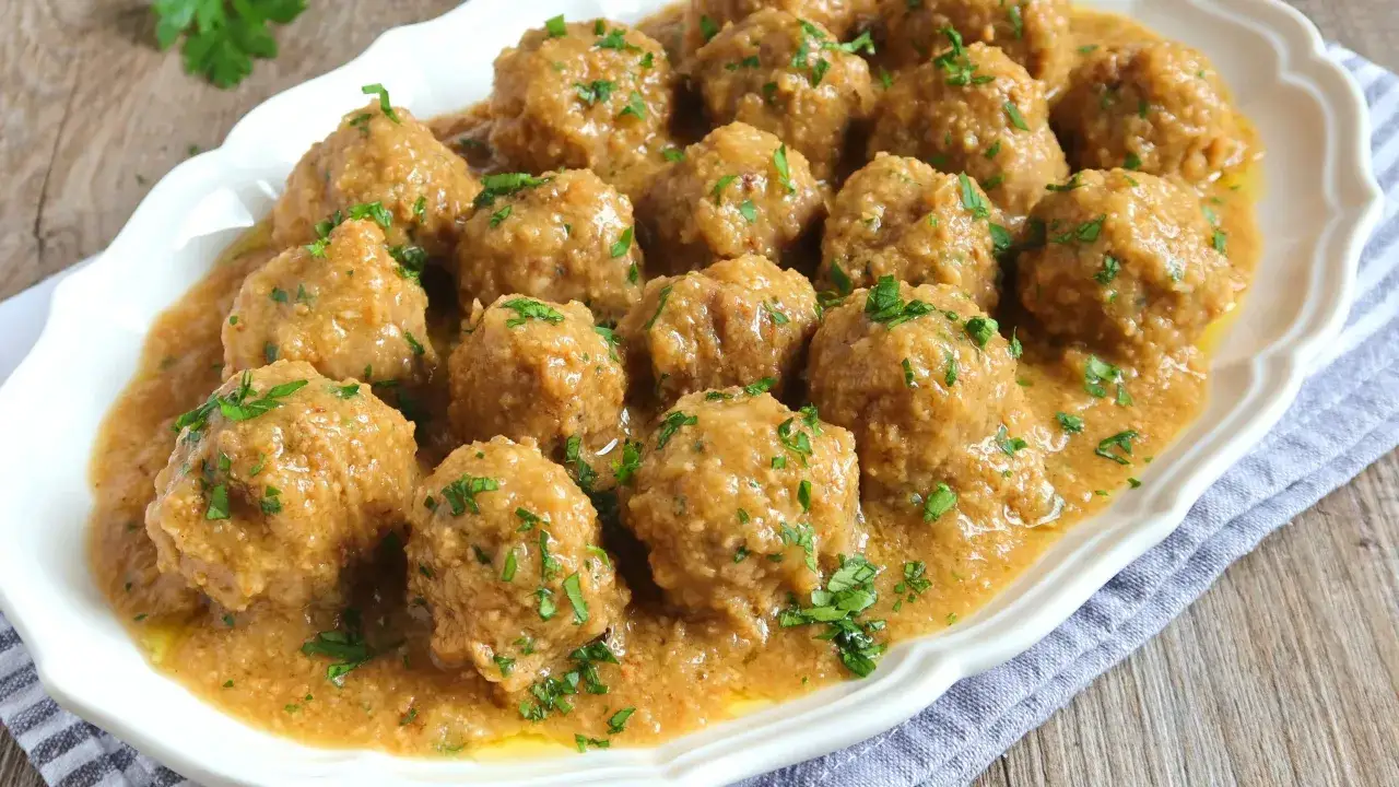 Albondigas en salsa de almendras, un plato casero con perejil fresco picado, servido en una fuente blanca.