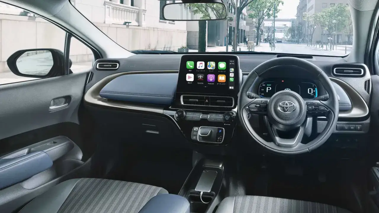 Wnętrze nowoczesnego Toyota Aqua z dużym ekranem dotykowym, cyfrowymi zegarami i wygodnymi siedzeniami.