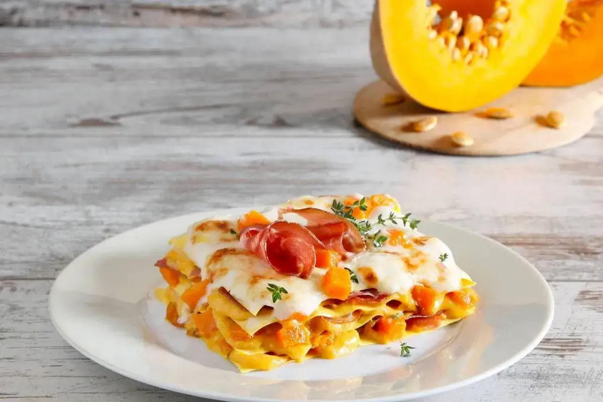 Lasagne con zucca e scamorza, un piatto autunnale ricco e saporito, guarnito con prosciutto crudo e timo.
