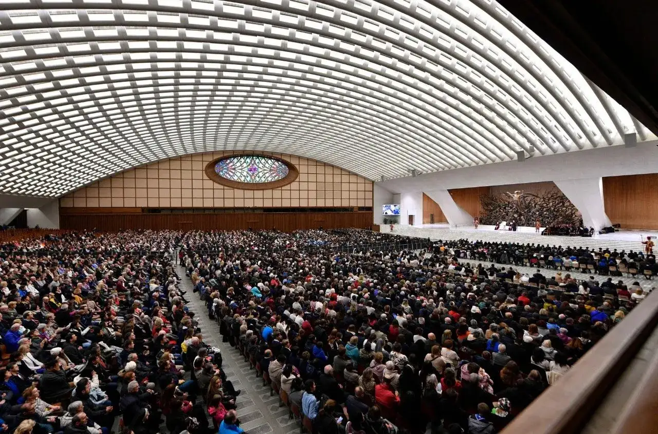 Der Papst spricht zu einer riesigen Menschenmenge in einer modernen Audienzhalle. Was macht der Papst den ganzen Tag? Er inspiriert und leitet Gläubige.
