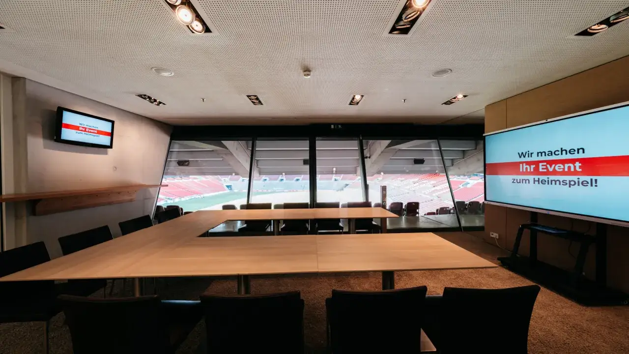 Konferenzraum mit Blick auf ein Stadion. Ein gro&szlig;er Tisch und St&uuml;hle stehen bereit, um Ihr Event zum Heimspiel zu machen.
