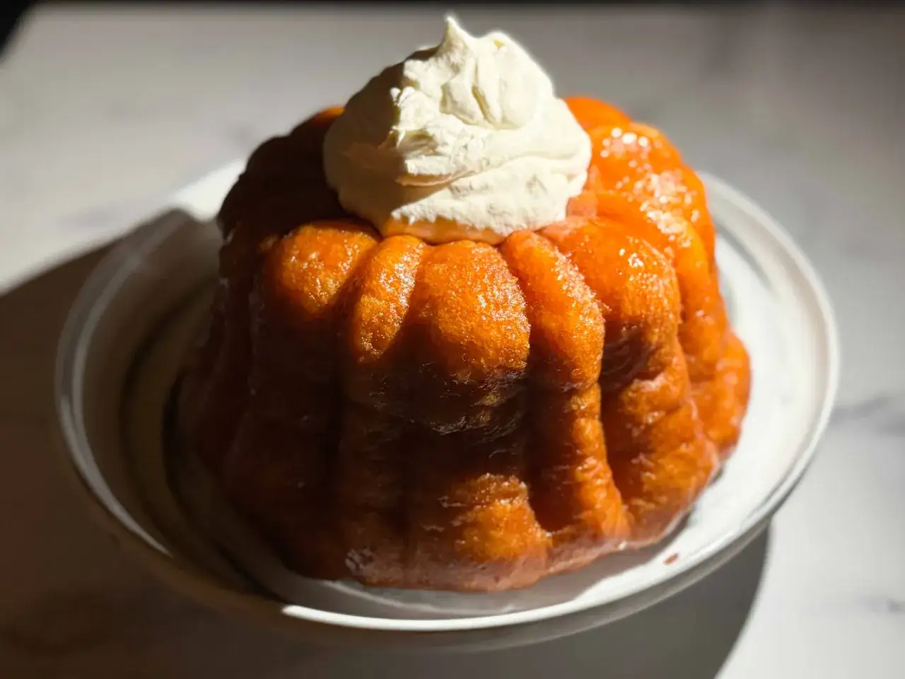 Ein gl&auml;nzender Baba au Rhum, getoppt mit einer Sahnehaube, auf einem Teller.