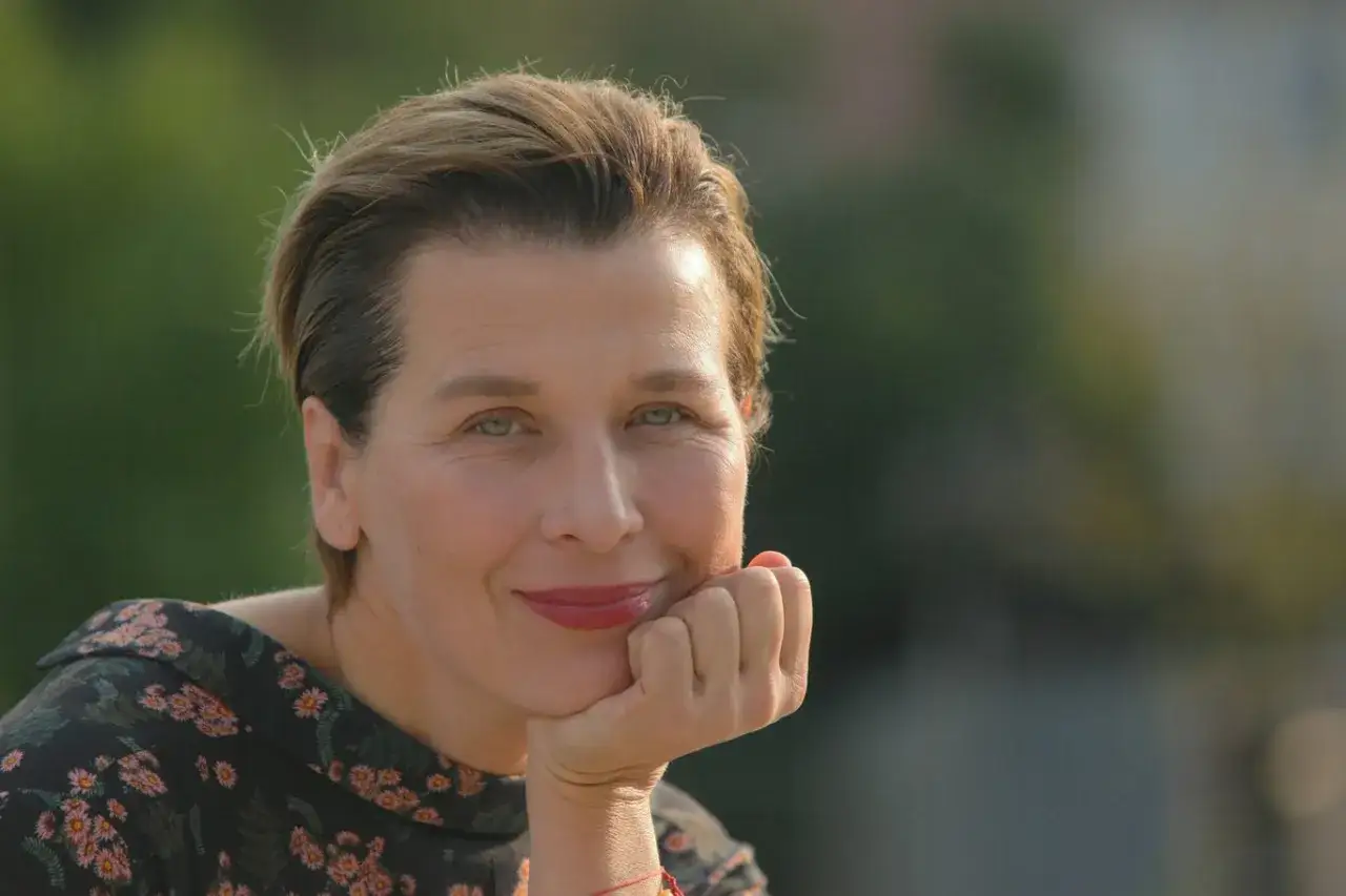 Katarzyna Herman chora, ale z uśmiechem na twarzy, opiera głowę na dłoni.