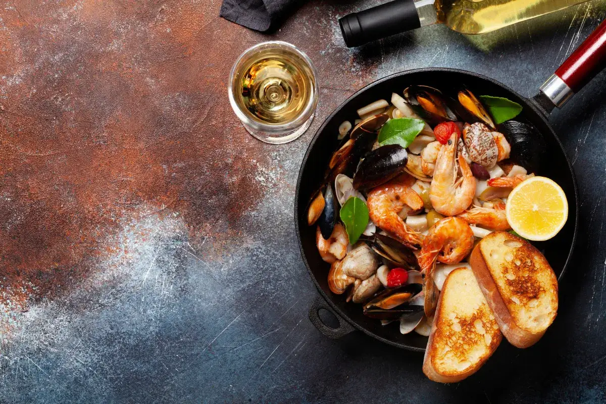 Un plat de fruits de mer savoureux avec crevettes, moules et palourdes, accompagné de pain grillé et d'une tranche de citron. Le parfait exemple de quel vin avec fruits de mer.
