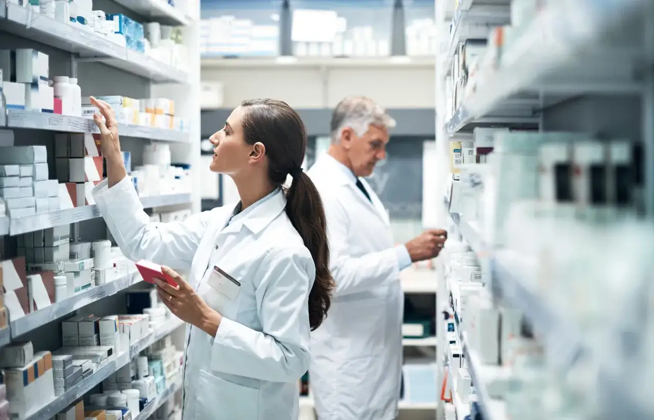 Farmaceuta w białym fartuchu wybiera lek z półki. Zastanawiasz się, ile zarabia technik farmacji?