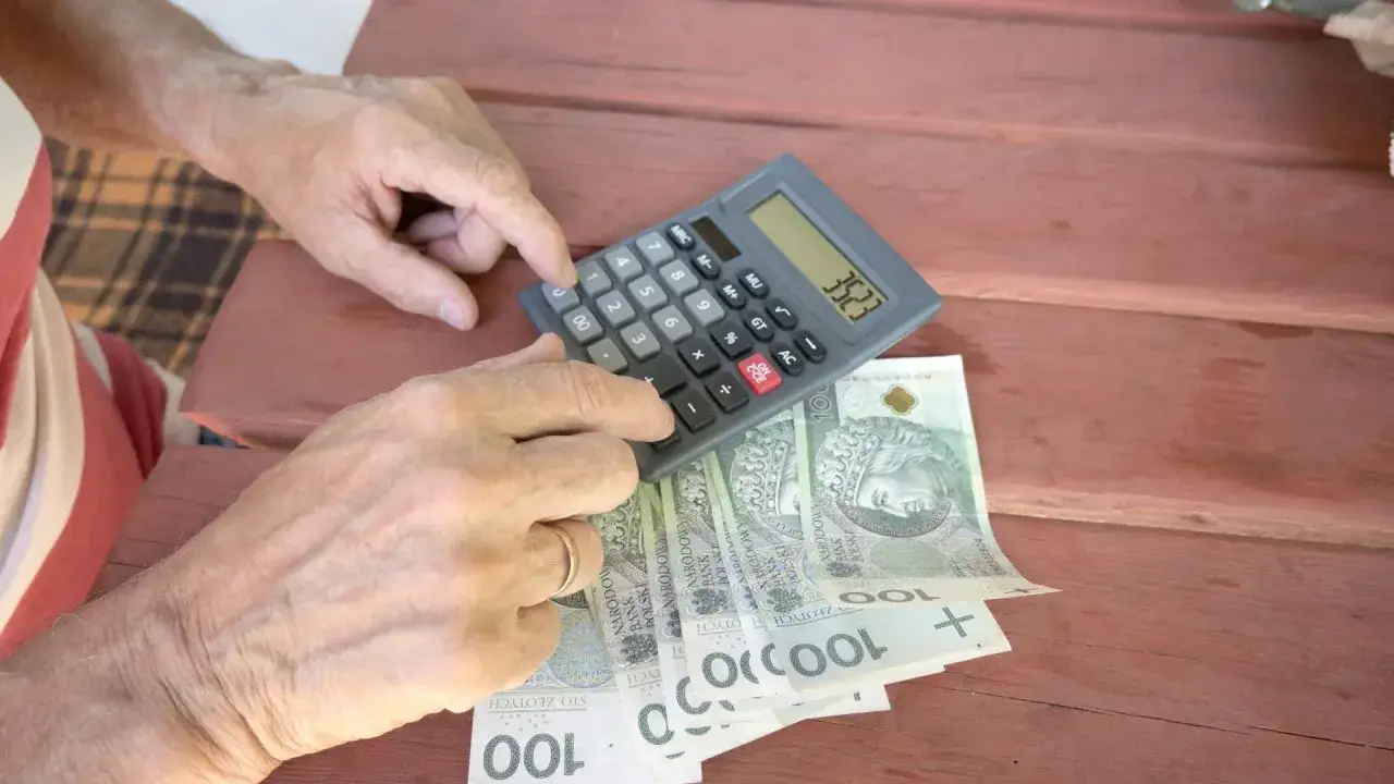 Ręce liczą pieniądze na kalkulatorze, planując wcześniejszą emeryturę. Polskie banknoty leżą obok.