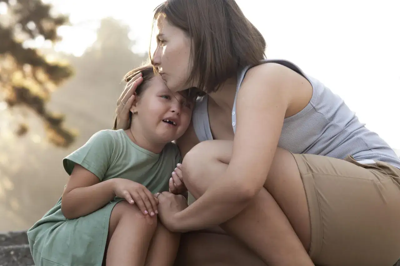 Un tenero abbraccio tra madre e figlia, un momento di conforto e attaccamento affettivo. La mamma bacia la fronte della bambina che piange, consolandola.