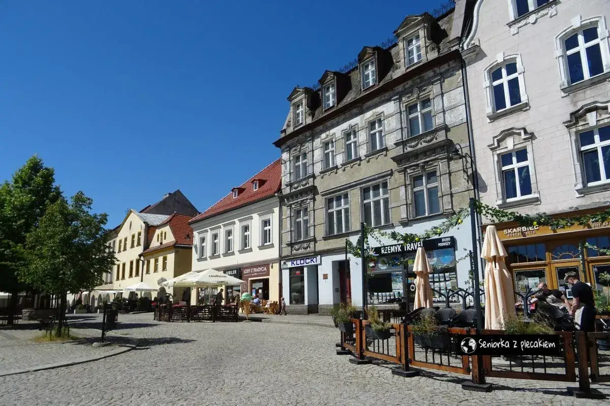 Tarnowskie Góry atrakcje: Rynek z kamienicami, kawiarniami i zielenią. Słoneczny dzień zachęca do spaceru i podziwiania urokliwego placu.