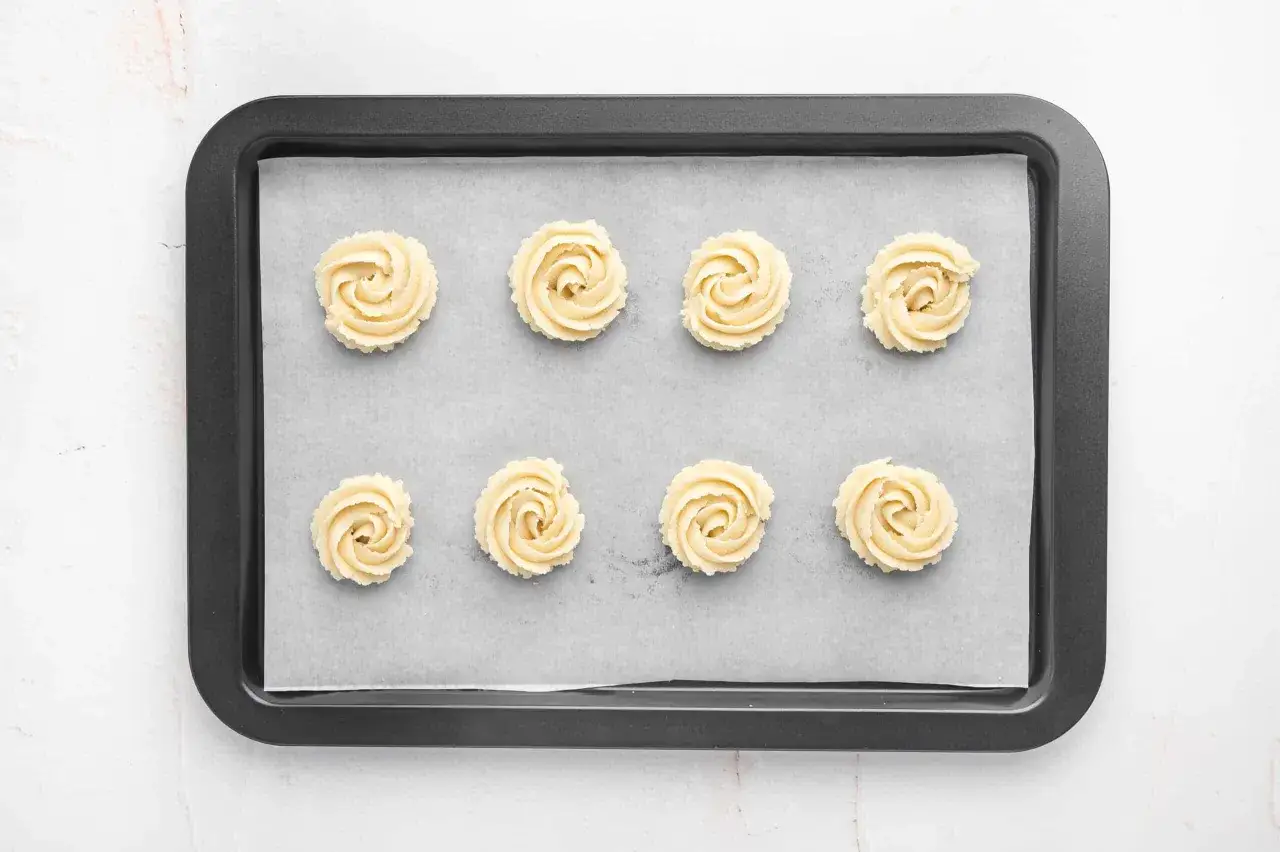 Ocho galletas de mantequilla con forma de roseta listas para hornear. Aprende como hacer galletas caseras perfectas.