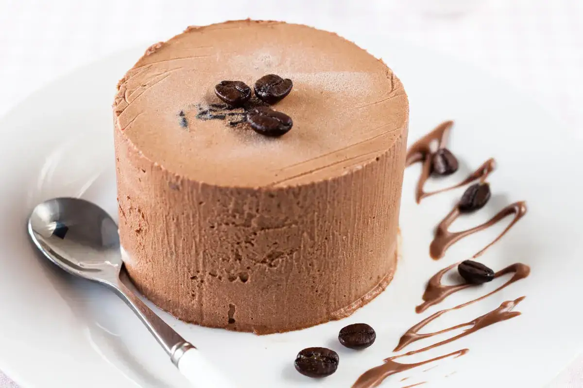 Delizioso semifreddo al caffè, guarnito con chicchi di caffè e salsa al cioccolato su un piatto bianco, pronto per essere gustato con un cucchiaino.
