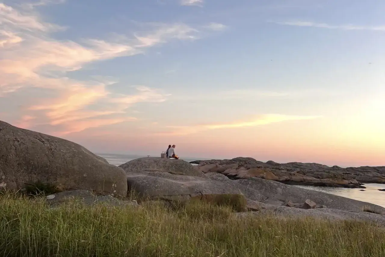 Två personer njuter av en picknick vid havet vid Solvik Kungshamn under en vacker solnedgång.