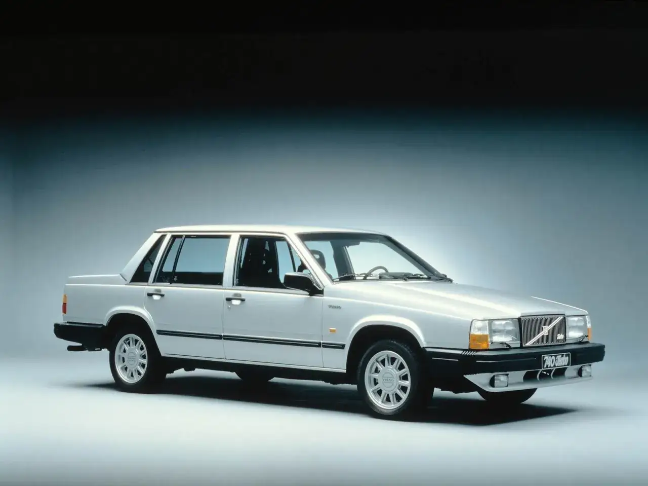En silverfärgad, gammal Volvo 740 Turbo står uppställd i en studio. Bilen har en klassisk, kantig design.