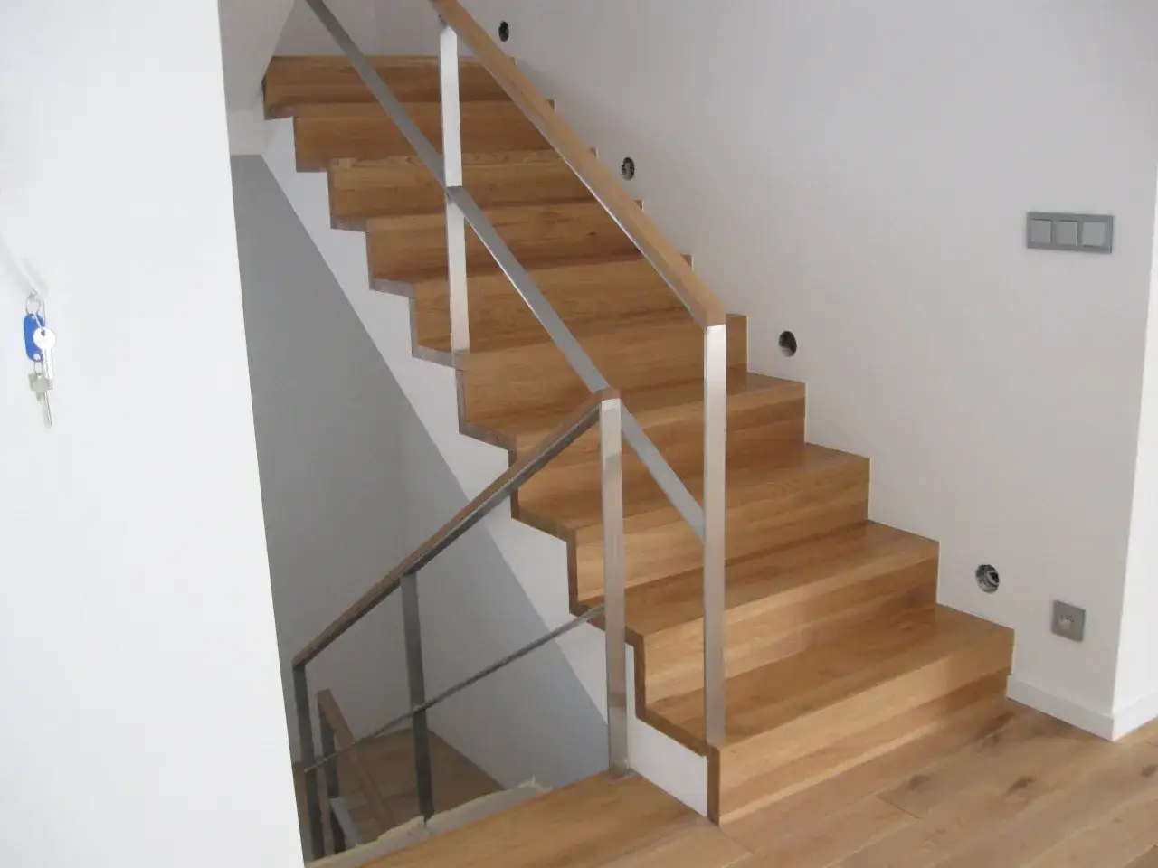 Drewniane schody dywanowe na beton z metalową balustradą. Nowoczesne, jasne wnętrze.