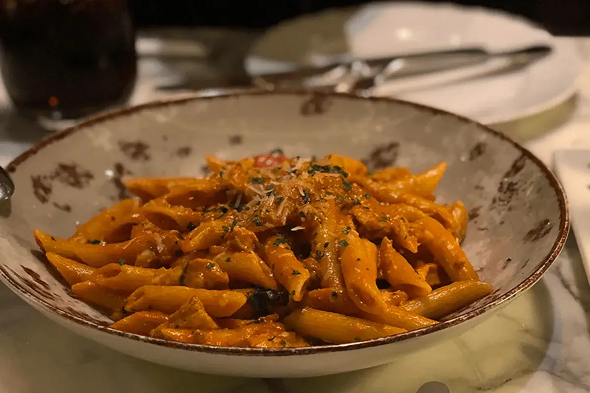 Penne al dente condite con una ricca pasta con crema di melanzane, guarnita con erbe fresche e parmigiano.