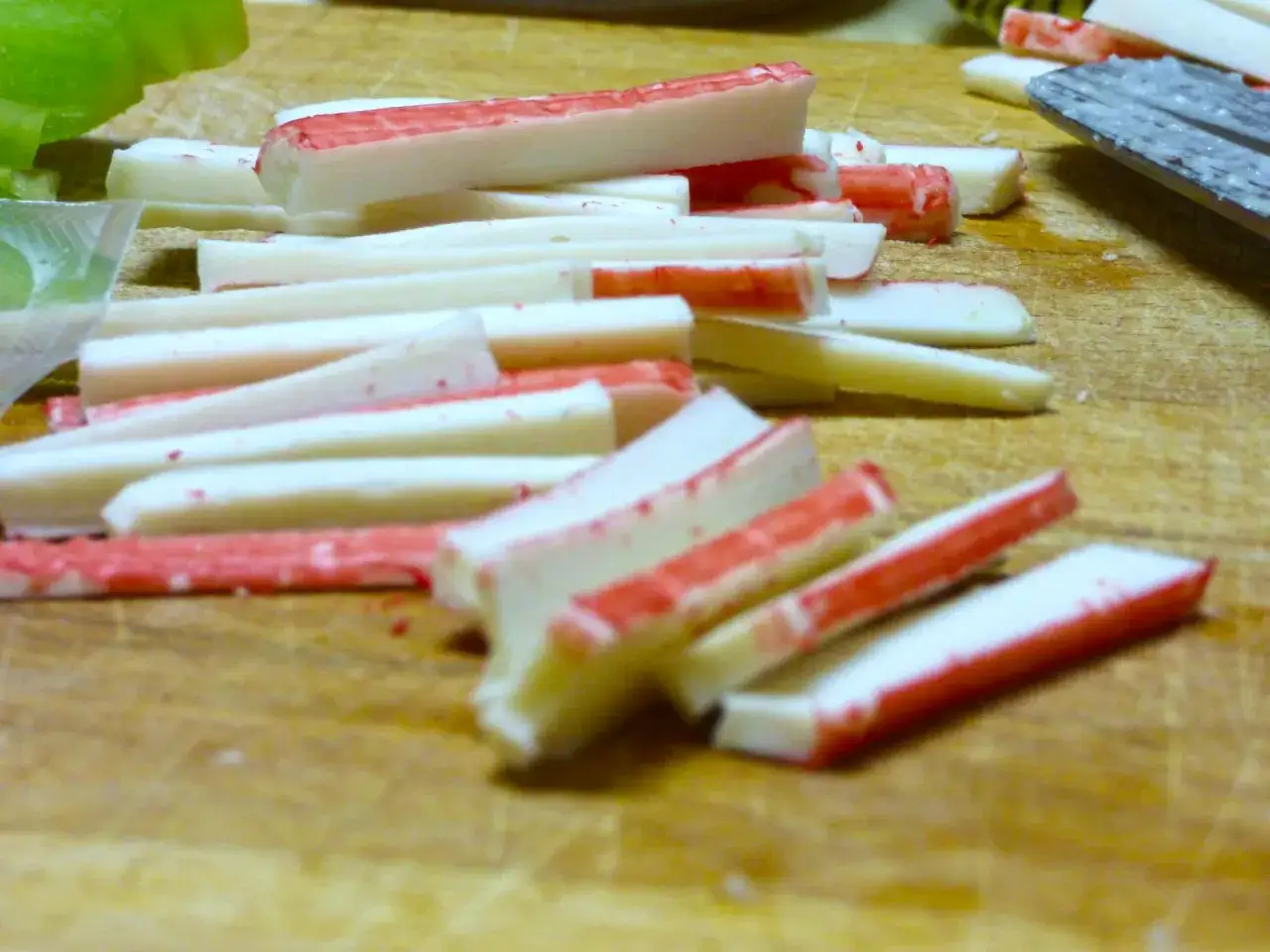 Paluszki surimi, czyli co to jest? Białe i czerwone kawałki na desce do krojenia, gotowe do sałatki.