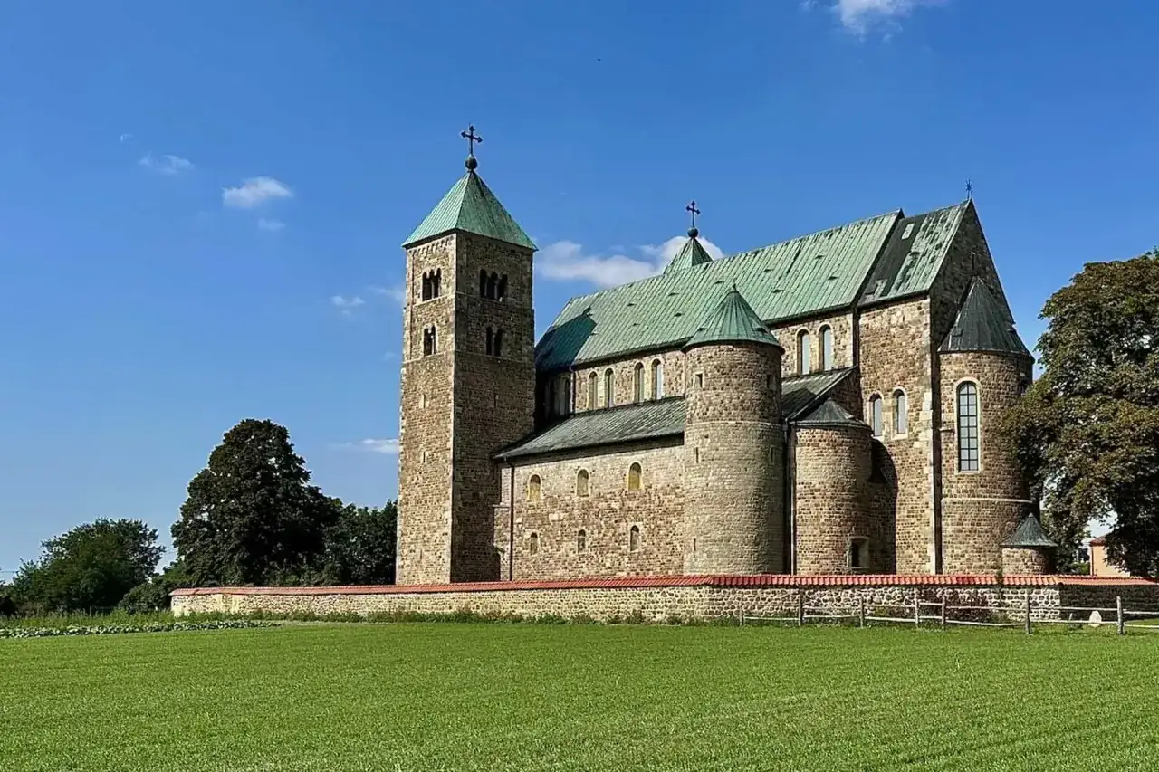 Kamienna budowla z zielonym dachem, przypominająca dawne grodzisko w Tumie, stoi na tle błękitnego nieba.