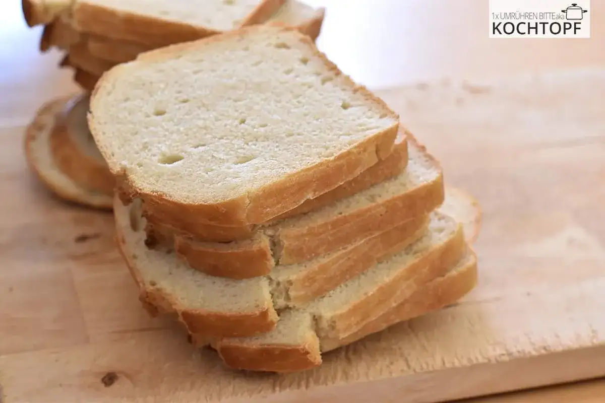 Gestapelte Scheiben von hellem Sandwichbrot liegen auf einem Holzbrett. Perfekt für Toast oder belegte Brote.