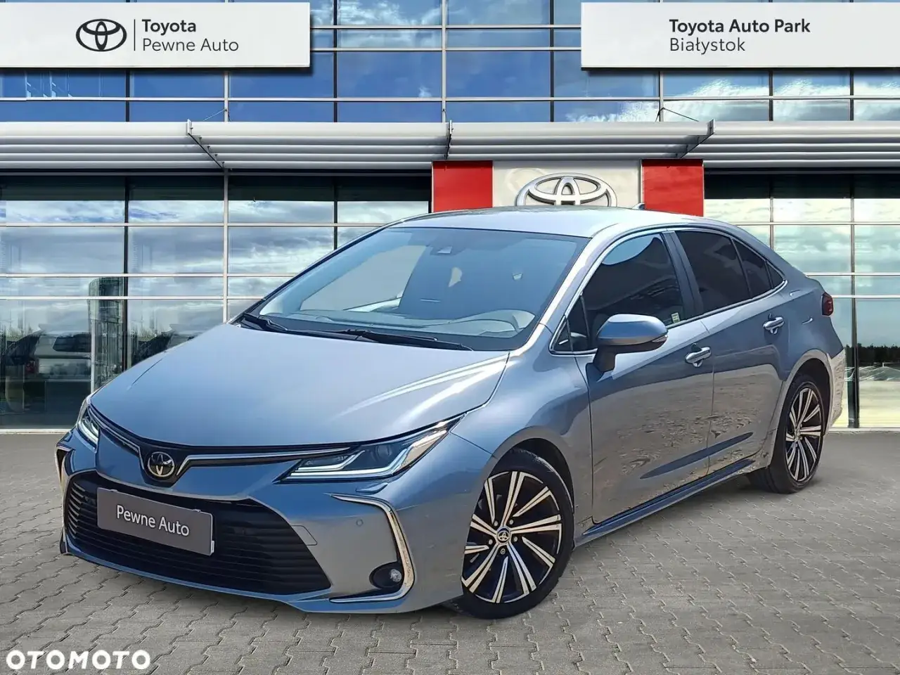 Szary sedan Toyota Corolla na tle salonu Toyota Auto Park. Idealny do codziennych podróży i rodzinnych wyjazdów, ten model jest gotowy na Twój toyota corolla test.