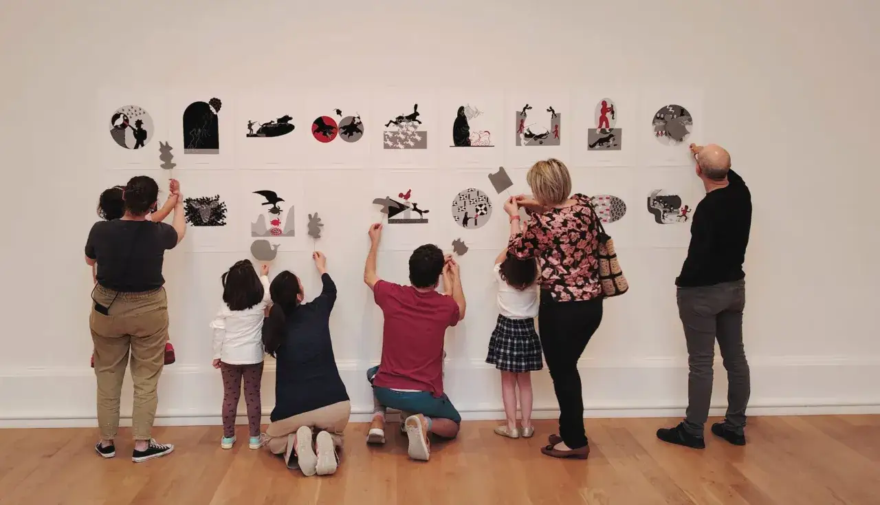 Familia interactuando con una exposición de siluetas en Bilbao con niños. Las obras muestran escenas fantásticas y animales.